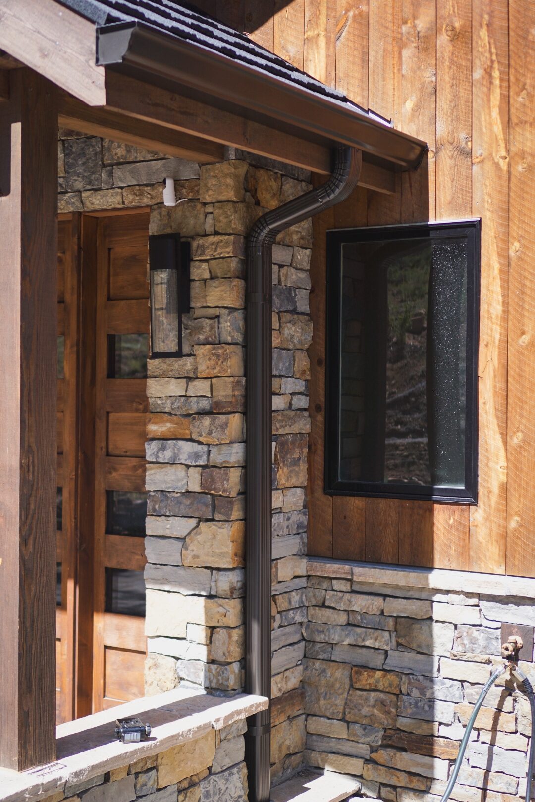 Bronze seamless gutter and downspout run from roof to grade next to the stone entry column of a Colorado mountain-modern home.