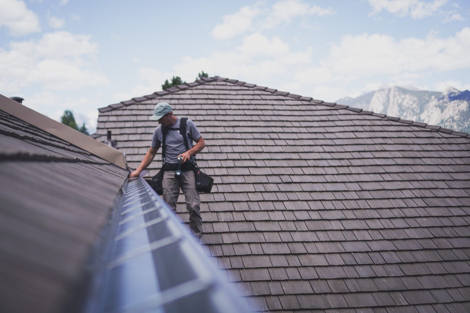 Green Brothers Gutters installer setting seamless aluminum gutters on the cedar-shake roof of a Colorado Front Range home, with the Rocky Mountains in the background.